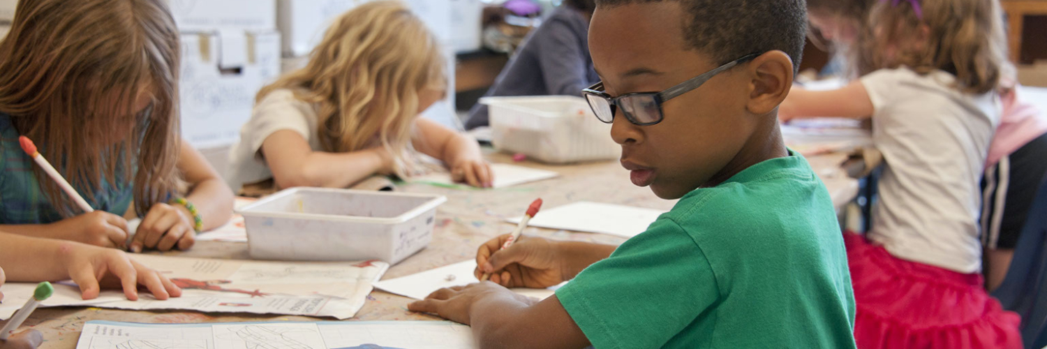 Children along a long desk, writing on pieces of paper